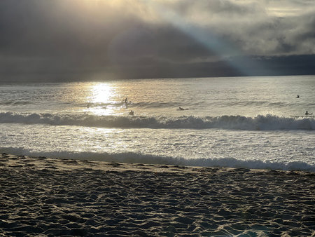 Surfers Catching Waves at Sunset Along a Tranquil Beach With Soft Sand and Calm Watersの写真素材