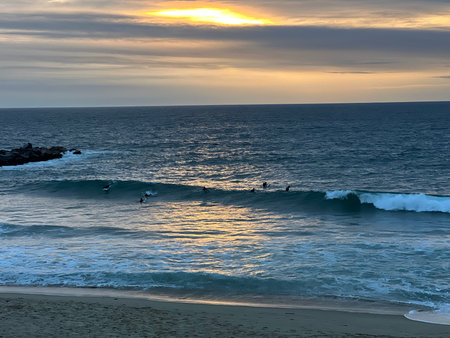 Surfing Enthusiasts Ride Waves as the Sun Sets Over the Ocean Horizon Near a Serene Beachの写真素材
