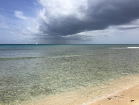 Waves Gently Lap Against the Sandy Shore as Clouds Gather Over the Peaceful Waters Near the Coastの写真素材