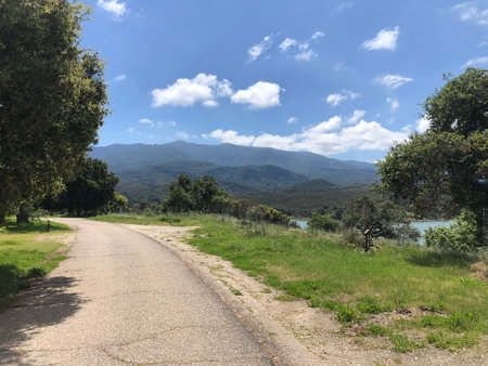 Scenic Pathway Leads to Mountains and Blue Sky in a Peaceful Countryside Settingの写真素材