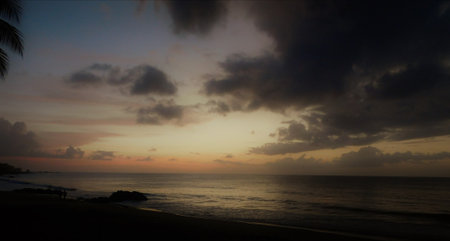 Sunset Over the Tranquil Beach With Dark Clouds Reflecting Hues of Orange and Purpleの写真素材
