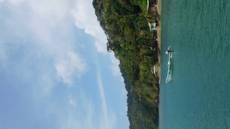Fishing Boat Navigates Calm Waters Near Lush Green Hills of a Tropical Paradise at Middayの写真素材