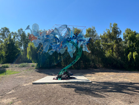 Vibrant Metal Tree Sculpture Stands Tall Under Clear Blue Skies in a Serene Park Settingの写真素材
