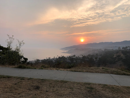Sunset Reflects on Calm Ocean Waves as Nature Paints the Sky With Warm Hues Over Coastal Hillsの写真素材