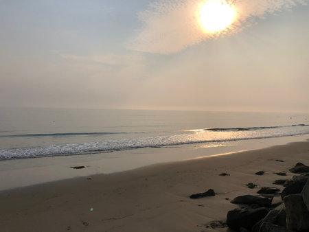 Serenity at Dawn as the Sun Rises Over the Calm Ocean Waves on a Quiet Beachの写真素材