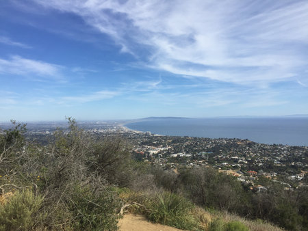 Scenic View of a Coastal City With Lush Hills and a Vast Ocean Under a Bright Skyの写真素材