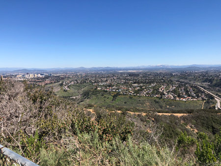 Sunny Day View From the Hillside Overlooking a Vibrant Cityscape and Distant Mountains During Middayの写真素材