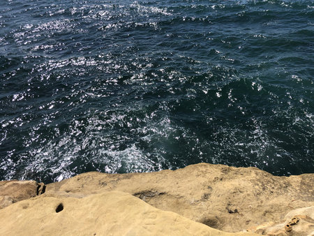 Waves Crashing Against Rugged Cliffs Under a Bright Sun in a Coastal Paradiseの写真素材