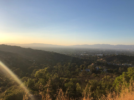 Sunset Over the Hills Showcasing a Vibrant Landscape and City Below Bathed in Golden Lightの写真素材