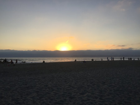 Golden Horizon Meets Gentle Waves at Sunset With Silhouettes of People Enjoying the Beach in the Evening Glowの写真素材
