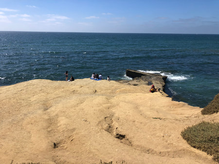 People Enjoying a Sunny Day at a Rocky Shoreline Overlooking the Ocean Wavesの写真素材