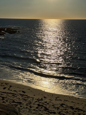 Calm Waves Lapping Against the Shore Under a Glowing Sunset Over the Oceanの写真素材