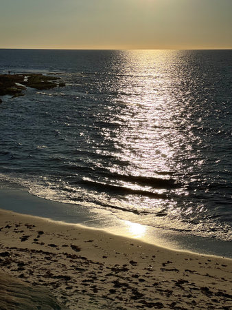 Serene Sunset Over the Calm Ocean Reflecting Shimmering Golden Light on the Tranquil Beachの写真素材