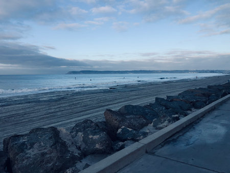 Morning Tranquility at the Beach With Gentle Waves and Surfers Enjoying the Calm Watersの写真素材