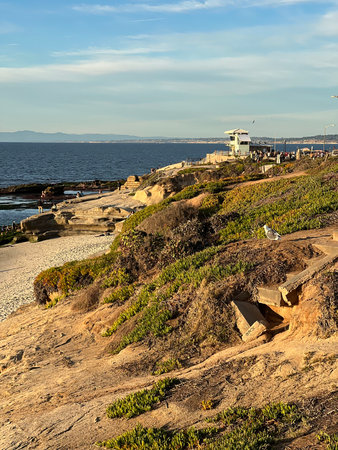 Sunset Over the Rocky Shore at La Jolla With Gentle Waves and Distant Beachgoers Enjoying a Peaceful Eveningの写真素材