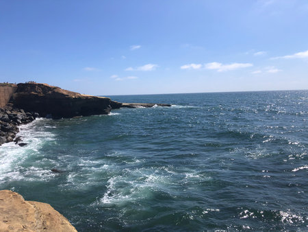 Waves Crashing Against Rocky Shore Under a Bright Blue Sky in a Peaceful Coastal Settingの写真素材