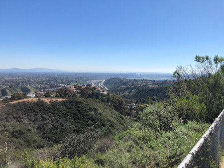 Expansive View of the Valley and Mountains From a Hilltop Trail Overlooking a Sprawling City Landscape Under a Clear Skyの写真素材