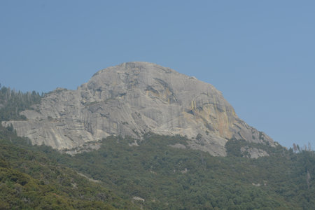 Majestic Granite Peak Rises Above the Lush Forest Under a Clear Blue Sky in the Afternoon Sunの写真素材