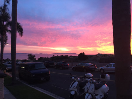 Vibrant Sunset Paints the Sky in Warm Hues Over a Coastal Parking Lot Surrounded by Palm Treesの写真素材