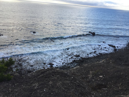 Waves Crashing Onto Rocky Shore at Dusk Near a Coastal Cliffの写真素材