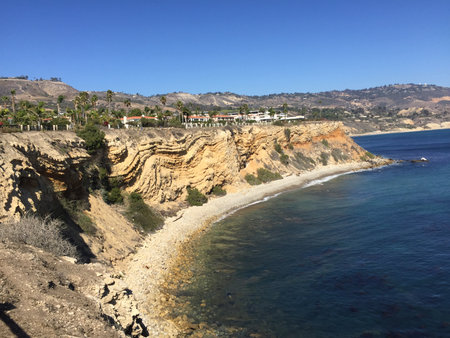 Sunlit Coastal Cliffs Offering a Stunning View of the Ocean and Waves Beneath a Clear Blue Sky Near a Serene Beachの写真素材