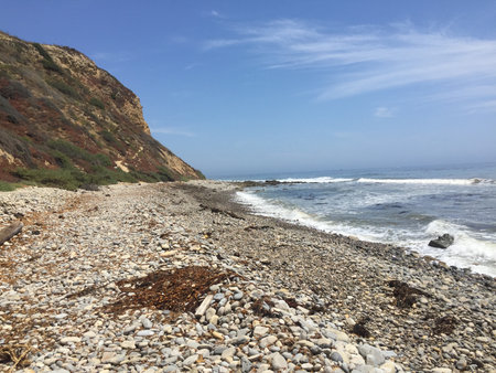 Serene Beach Landscape Featuring Smooth Pebbles and Gentle Waves Beneath a Bright Blue Skyの写真素材