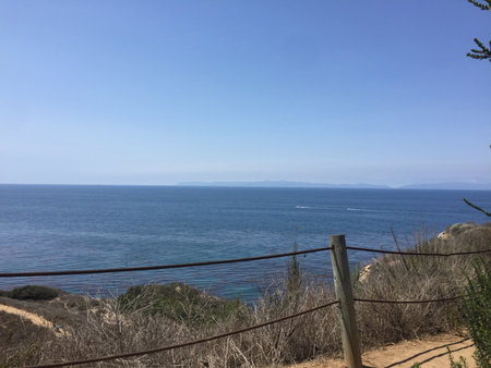 Serene Coastal View From a Hillside Path on a Sunny Day, Capturing the Endless Ocean and Distant Islandsの写真素材