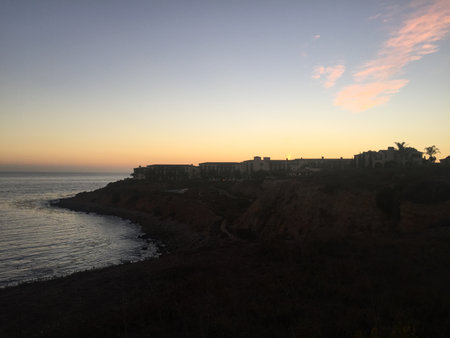 Serene Coastal Sunset Reflects Vibrant Hues Over Rocky Shoreline by Peaceful Oceanの写真素材