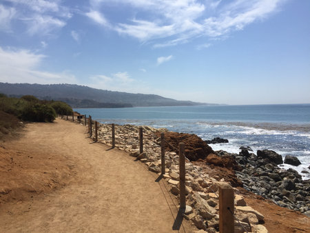 Winding Coastal Path by the Ocean With a Clear Blue Sky and Distant Mountains in the Warm Afternoon Lightの写真素材