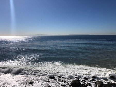 Captivating Waves Crash Against Rocky Shore Under a Clear Blue Sky at Sunset Near the Coastの写真素材