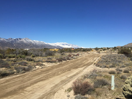 Scenic Desert Landscape Showcasing Dirt Path With Distant Mountains and Clear Blue Sky in a Rugged Terrainの写真素材