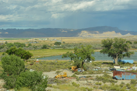 Vast Desert Landscape With Abandoned Vehicles Amidst Green Fields and Distant Mountains Under a Cloudy Skyの写真素材