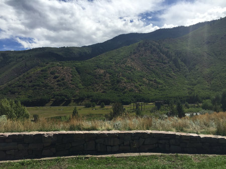 Scenic Mountain View With Vast Green Fields and Fluffy Clouds in the Bright Blue Sky During Early Afternoon in Serene Landscapeの写真素材