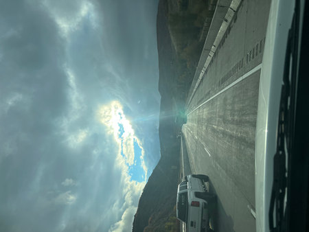 Sunlight Breaks Through Clouds Over a Winding Highway in the Mountains During a Scenic Driveの写真素材