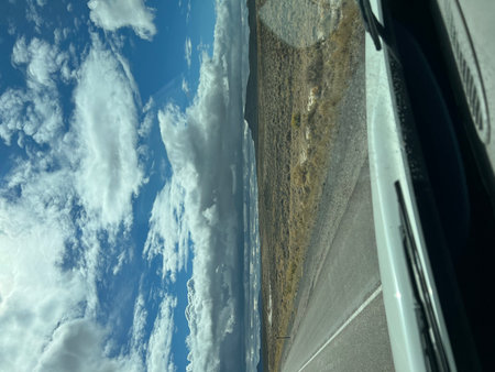 Scenic Drive Through Open Desert Landscape Under a Vast Sky Filled With Clouds Near a Distant Mountain Rangeの写真素材