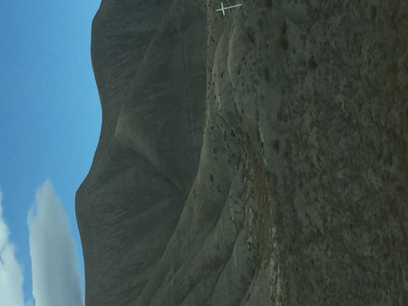 Cross on a Hillside Stands Tall Against a Dramatic Mountain Backdrop Under a Clear Blue Skyの写真素材