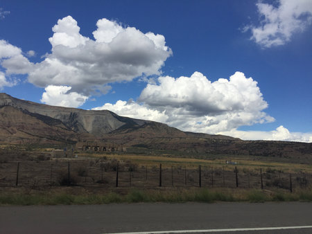 Majestic Mountains Rise Under a Bright Blue Sky With Fluffy White Clouds During a Serene Afternoon Driveの写真素材