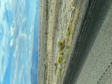 Vast Desert Landscape Under a Blue Sky With Scattered Clouds, Showcasing Serene Nature Along a Winding Roadの写真素材