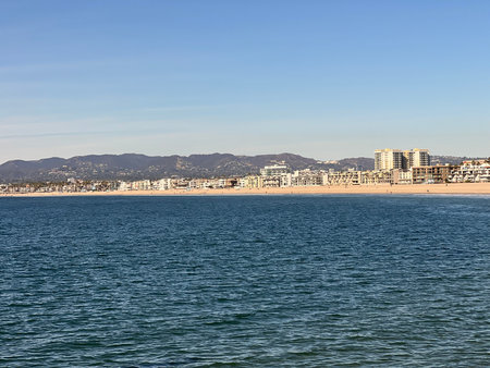 Coastal View of a Sunny Beach With Buildings and Mountains in the Distanceの写真素材