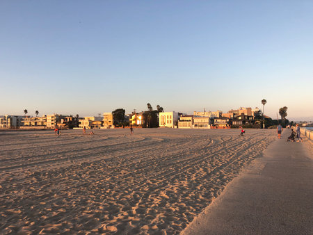 Golden Hour Over the Beach Showing Children Playing and People Strolling Along the Sand in a Coastal Townの写真素材