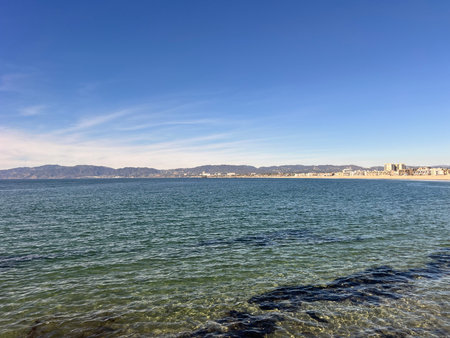 Coastal View Showcasing Clear Waters and Distant Mountains Under a Bright Blue Sky at Middayの写真素材