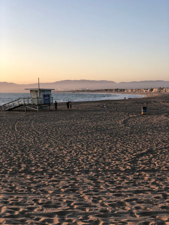 Sunset Stroll Along the Sandy Beach Under a Colorful Sky With Distant Mountains and Calm Waves Reflecting Twilight Huesの写真素材