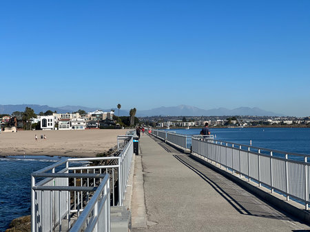 People Enjoy a Sunny Day Walking Along a Pier by the Ocean With Beautiful Mountains in the Backgroundの写真素材