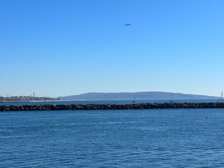 Beautiful Coastal View Featuring Calm Waters, Distant Hills, and a Plane Flying Overhead at Middayの写真素材
