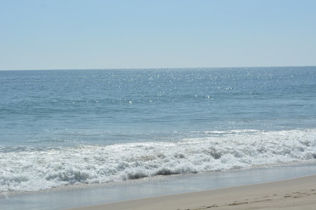 Sparkling Waves Gently Lap the Shore on a Sunny Day by the Coastの写真素材