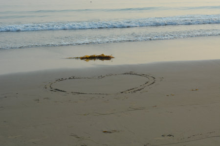 Creating a Heart in the Sand at the Beach During Sunset, a Peaceful Moment by the Ocean Wavesの写真素材