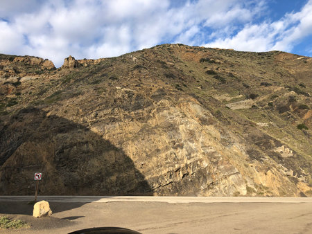Natural Rock Formation Rising Majestically Under a Vibrant Sky Near a Winding Mountain Roadの写真素材