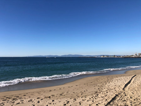 Tranquil Beach Scene With Golden Sand and Clear Blue Sky Overlooking Distant Mountains at Middayの写真素材