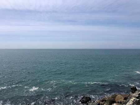Waves Gently Lap Against the Rocky Shore Under a Bright Blue Sky at Midday by the Oceanの写真素材