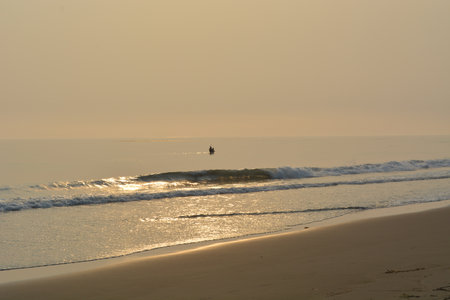 Calm Sunset at the Beach With a Lone Figure Fishing on Tranquil Watersの写真素材